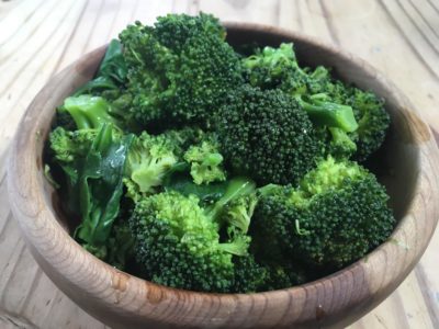 Close up view of a bowl of cooked broccoli. 